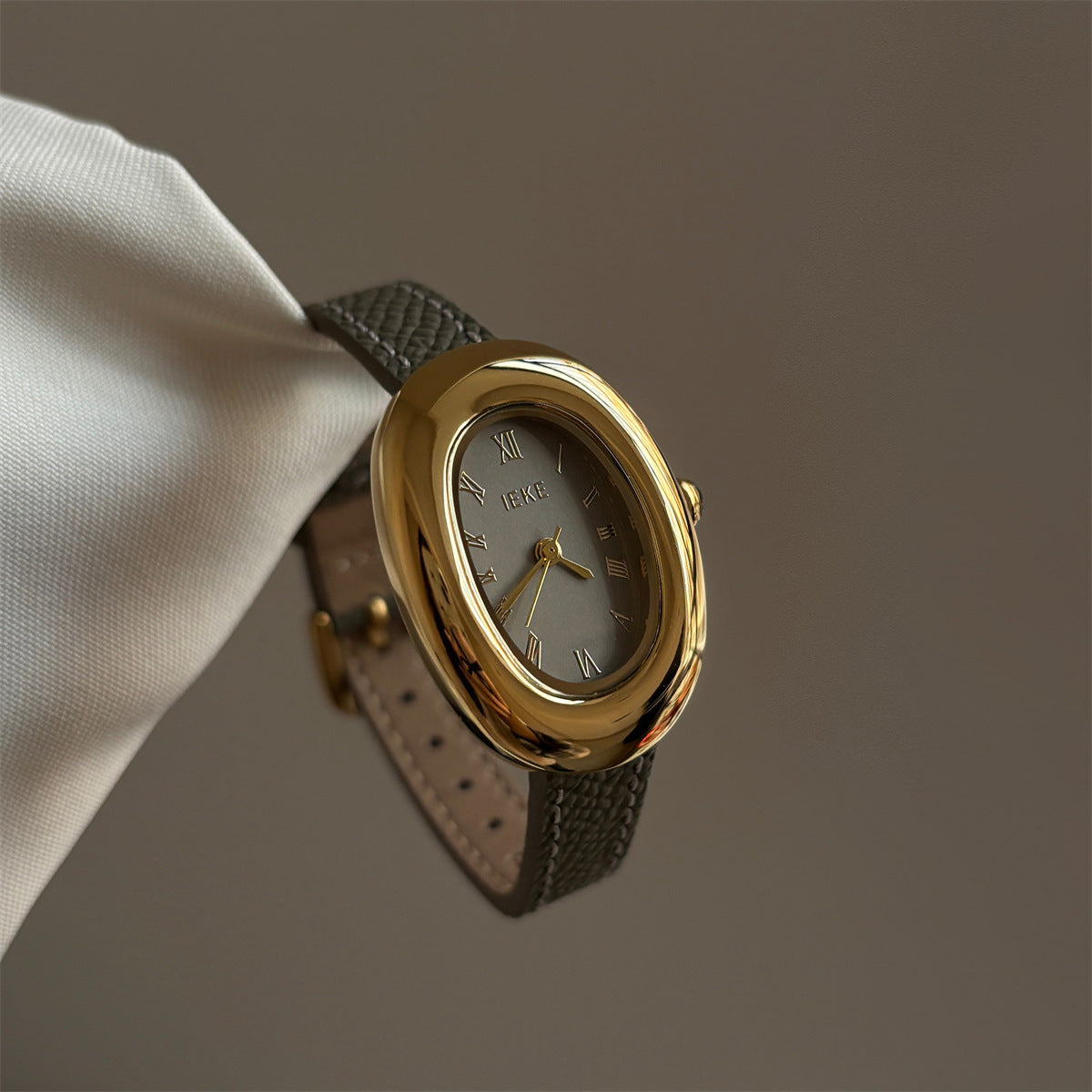 Olive-colored strap watch with a gold oval dial, featuring a niche design