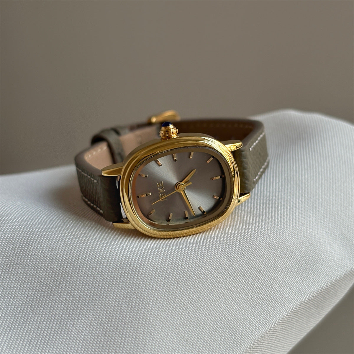 Olive-colored strap watch with a gold oval dial, featuring a niche design