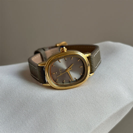 Olive-colored strap watch with a gold oval dial, featuring a niche design