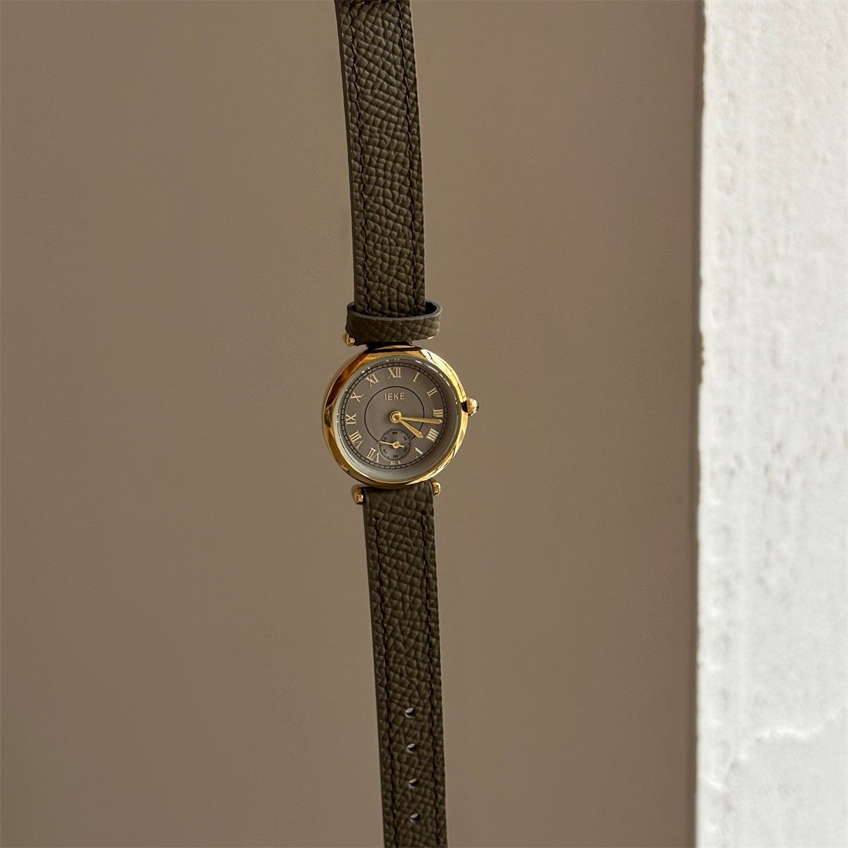 Olive-colored strap watch with a gold round dial, featuring a niche design