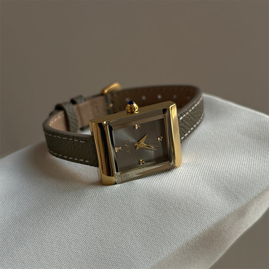 Olive-colored strap watch with a small gold square dial, featuring a niche design