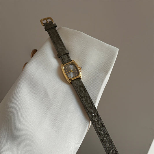 Olive-colored strap watch with a small gold square dial, featuring a niche design