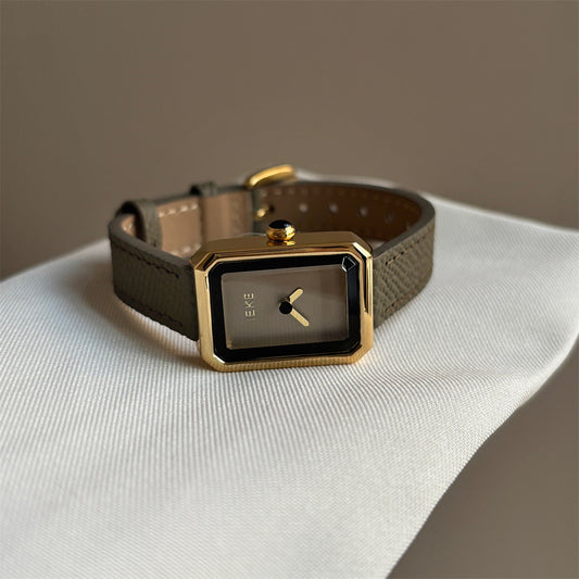 Olive-colored strap watch with a small gold square dial, featuring a niche design