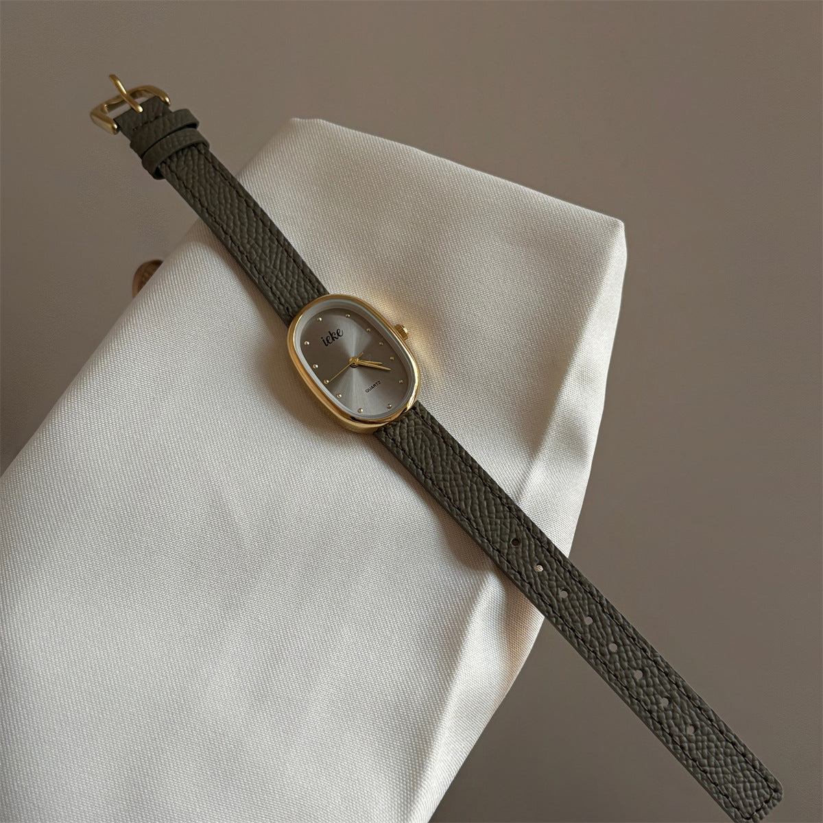 Olive-colored strap watch with a gold oval dial, featuring a niche design